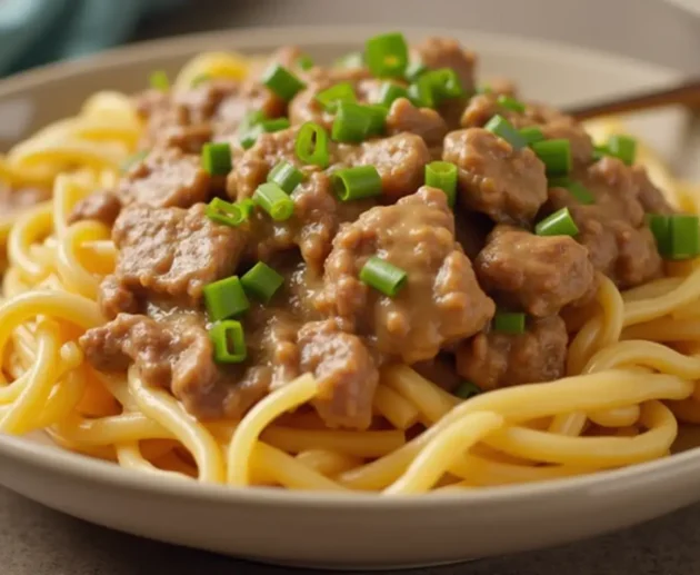 A freshly prepared Hamburger Helper Beef Stroganoff dish served in a white bowl on a wooden table. The creamy mushroom sauce, tender ground beef, and pasta spirals are garnished with fresh parsley, creating a warm and inviting presentation.