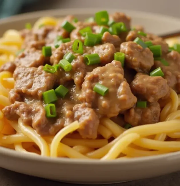 A freshly prepared Hamburger Helper Beef Stroganoff dish served in a white bowl on a wooden table. The creamy mushroom sauce, tender ground beef, and pasta spirals are garnished with fresh parsley, creating a warm and inviting presentation.