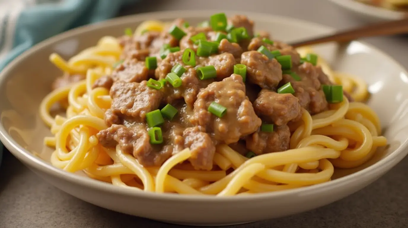 A freshly prepared Hamburger Helper Beef Stroganoff dish served in a white bowl on a wooden table. The creamy mushroom sauce, tender ground beef, and pasta spirals are garnished with fresh parsley, creating a warm and inviting presentation.